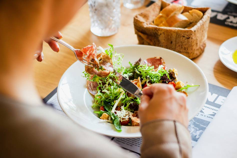 Person preparing a colorful bowl of gut-healthy foods like yogurt, berries, oats, and leafy greens